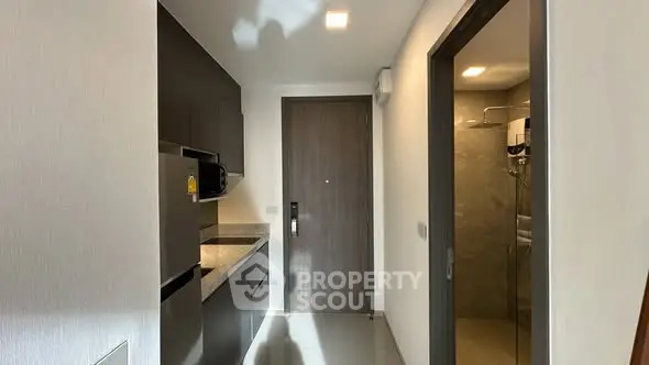 Modern apartment kitchen with sleek cabinetry and adjacent bathroom entrance.