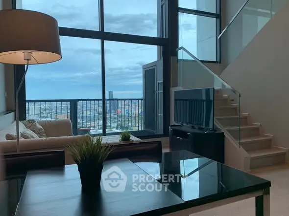 Modern living room with large windows and city view, featuring stylish furniture and a staircase.