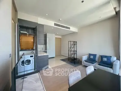 Modern open-plan living room with kitchen, featuring a washing machine and stylish furniture.