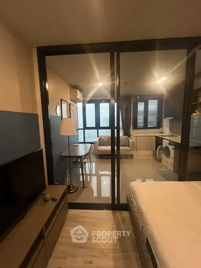 Modern studio apartment with glass partition, cozy living area, and compact kitchen featuring a washing machine.