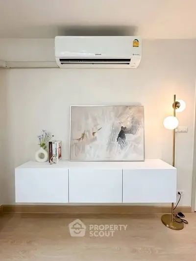 Modern living room with sleek white cabinet, stylish artwork, and elegant floor lamp under air conditioning unit.