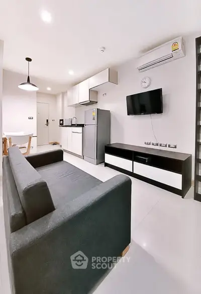 Modern open-layout living room with sleek kitchen, featuring a cozy sofa and wall-mounted TV.