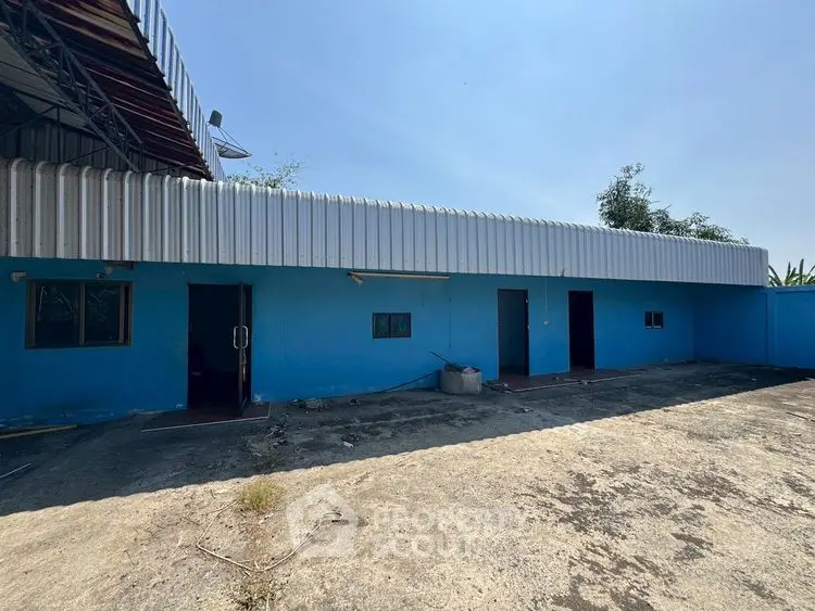Industrial building exterior with blue walls and corrugated metal roof, spacious outdoor area.
