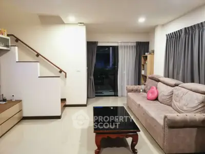 Modern living room with plush sofa and sleek coffee table, featuring elegant staircase and large window view.