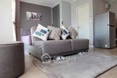 Modern living room with stylish sofa, cozy rug, and sleek refrigerator in open layout apartment.