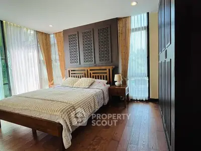 Spacious bedroom with elegant wooden flooring and large windows for natural light.