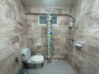 Spacious bathroom with modern shower and colorful curtain in a tiled setting.