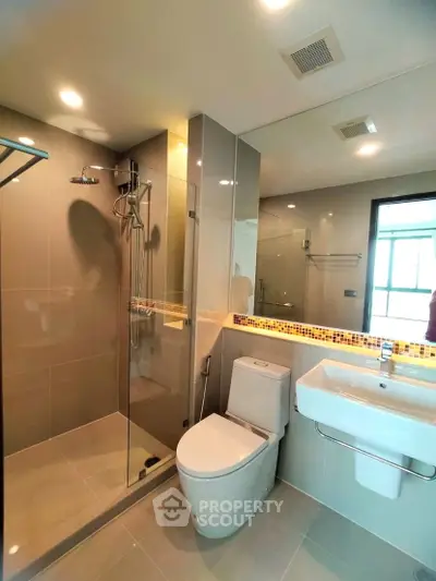 Modern bathroom with glass shower, sleek fixtures, and large mirror in a contemporary home.