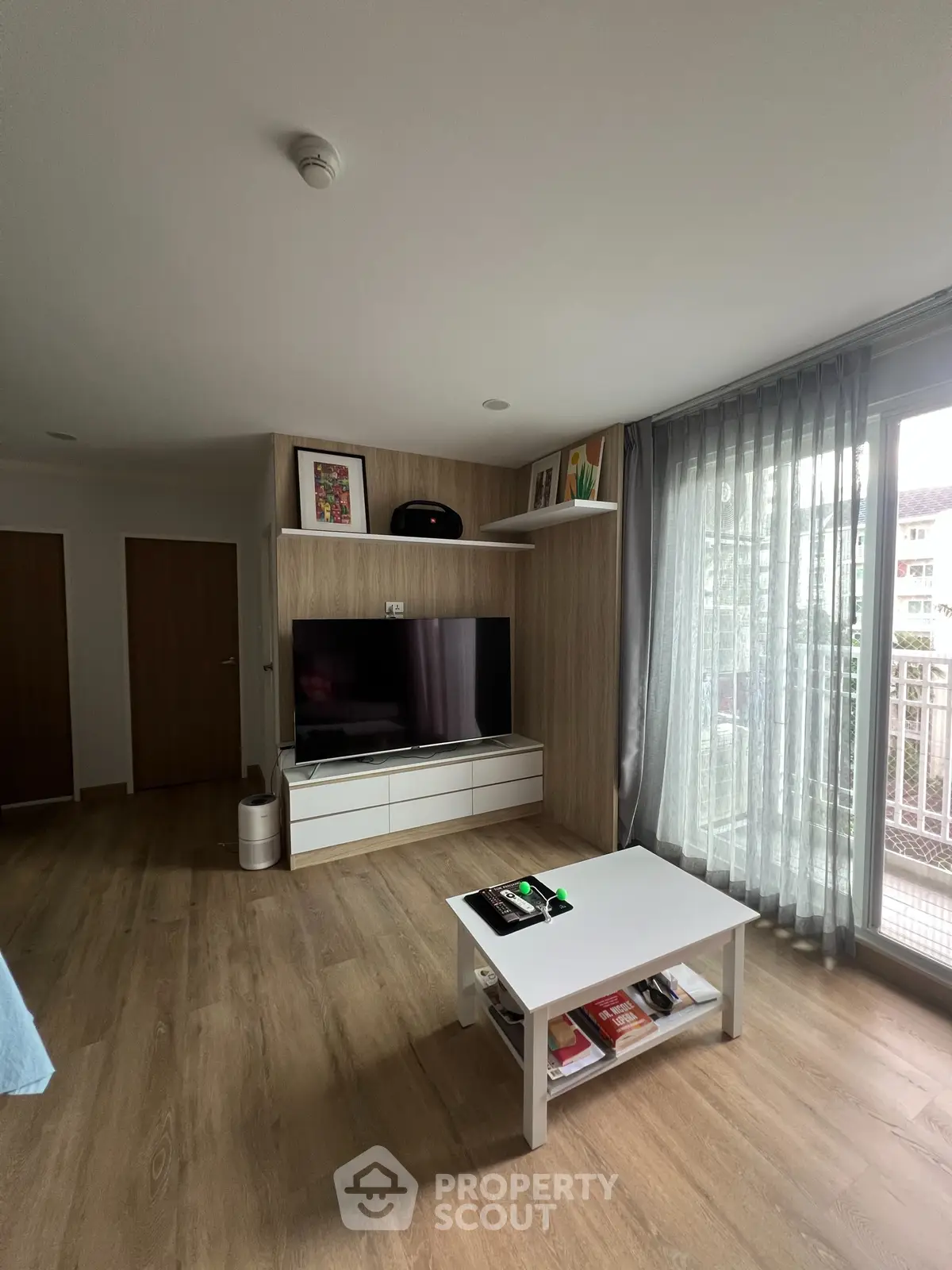 Spacious modern living room with large TV and balcony view, perfect for relaxation and entertainment.
