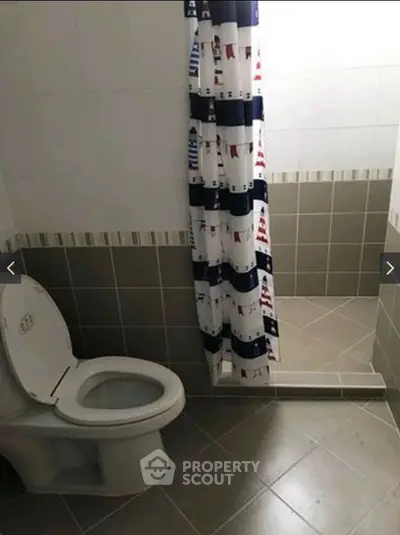 Modern bathroom with tiled floor and nautical-themed shower curtain.
