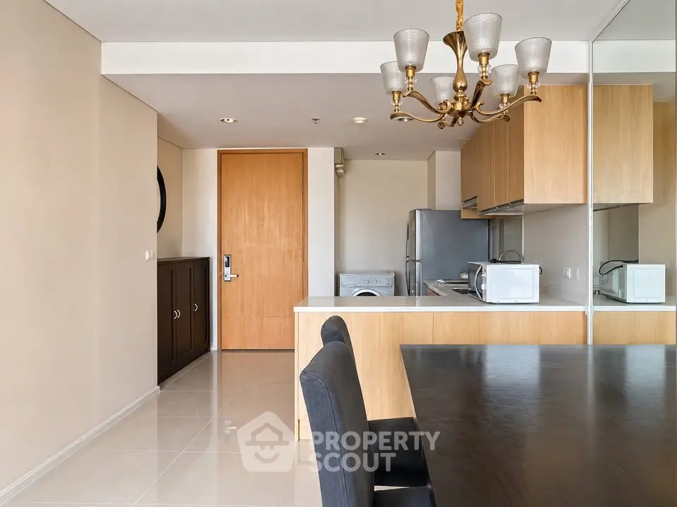 Modern kitchen with wooden cabinets, dining area, and elegant chandelier in a stylish apartment.