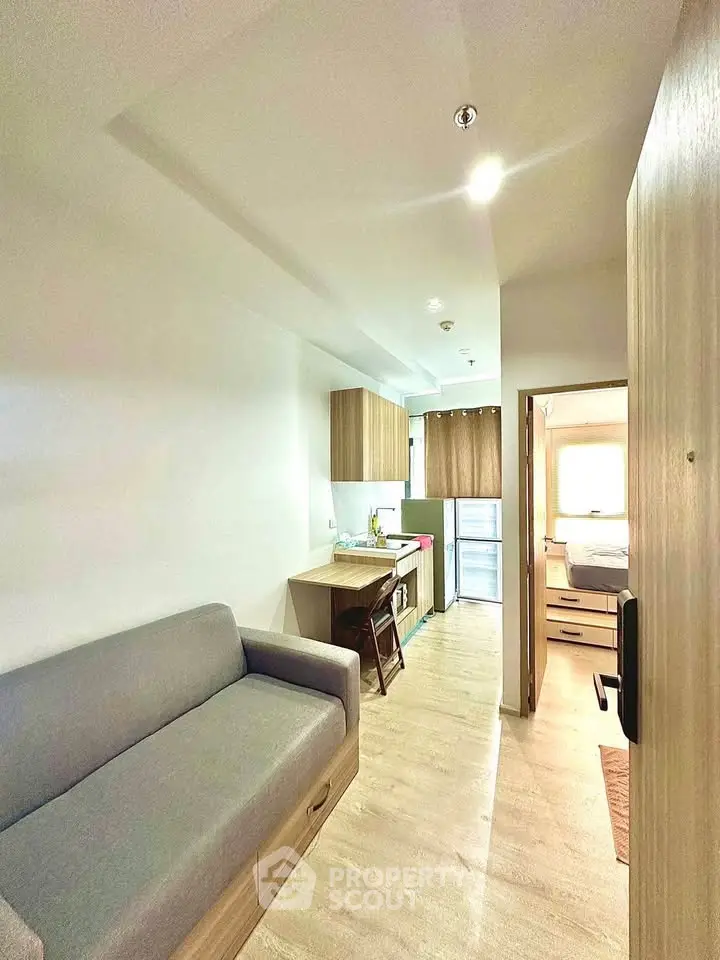 Modern studio apartment with cozy living area and compact kitchen, featuring sleek wooden cabinetry and natural light.
