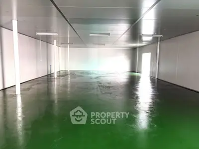 Spacious industrial warehouse with polished green flooring and high ceilings, ideal for storage or manufacturing.