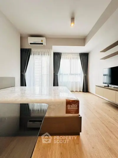 Spacious modern bedroom with large windows and wooden flooring, featuring a sleek TV setup and air conditioning.