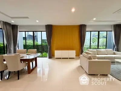 Spacious modern living room with elegant dining area and large windows overlooking greenery.