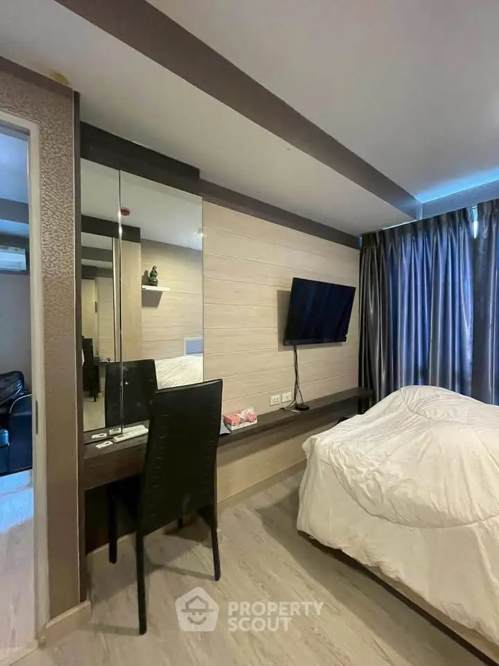 Modern bedroom with sleek design, featuring a wall-mounted TV, large mirror, and stylish furnishings.