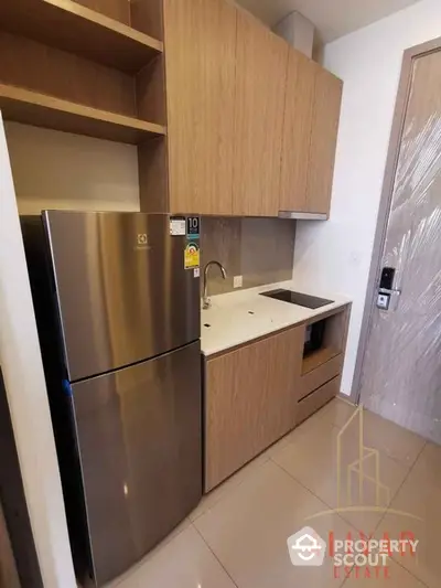 Compact modern kitchen with stainless steel refrigerator, built-in oven, and wooden cabinetry, perfect for urban living.