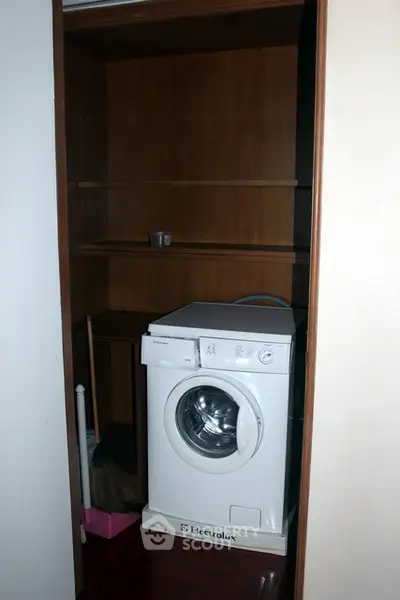 Compact laundry nook with Electrolux washing machine and wooden shelving.