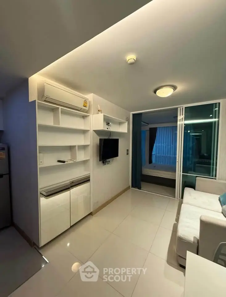 Modern living room with sleek design and built-in storage, leading to a cozy bedroom.