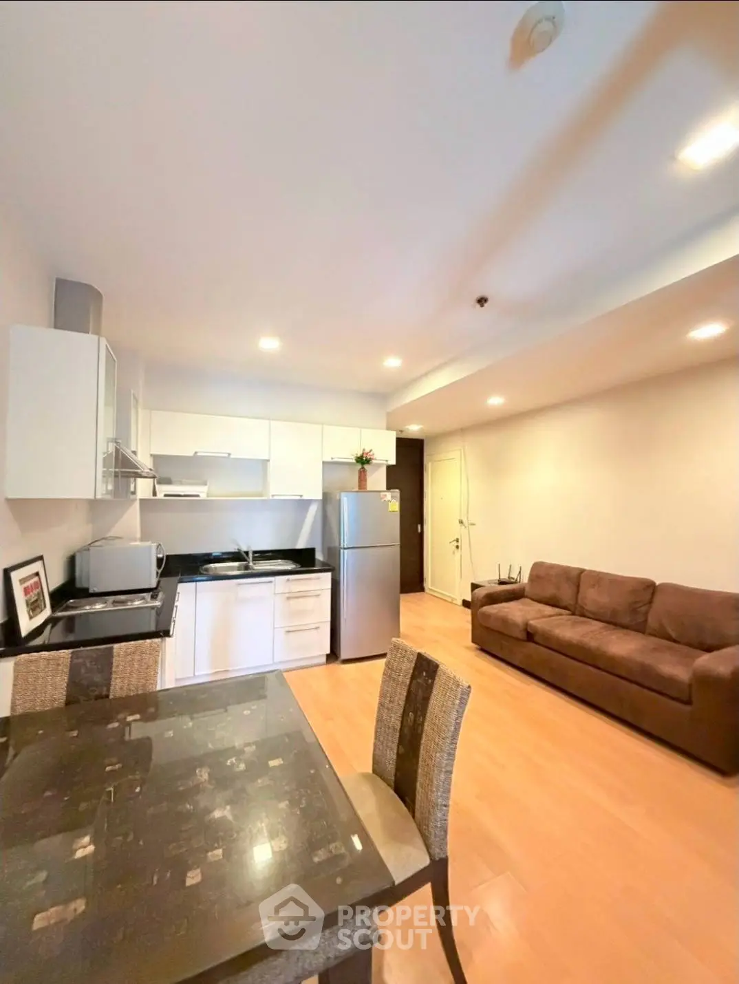 Modern open-layout living room with kitchen, featuring sleek furniture and bright lighting.