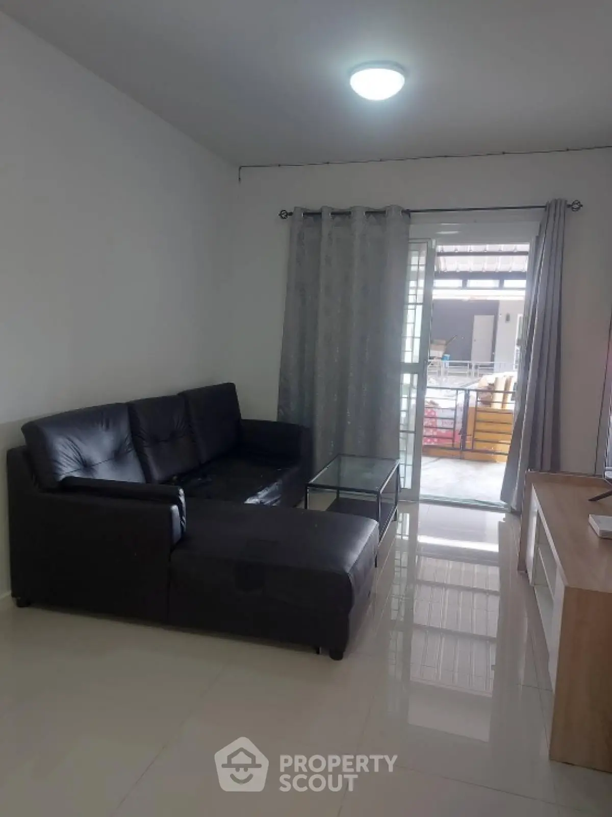 Modern living room with sleek black sofa and glass coffee table near balcony.