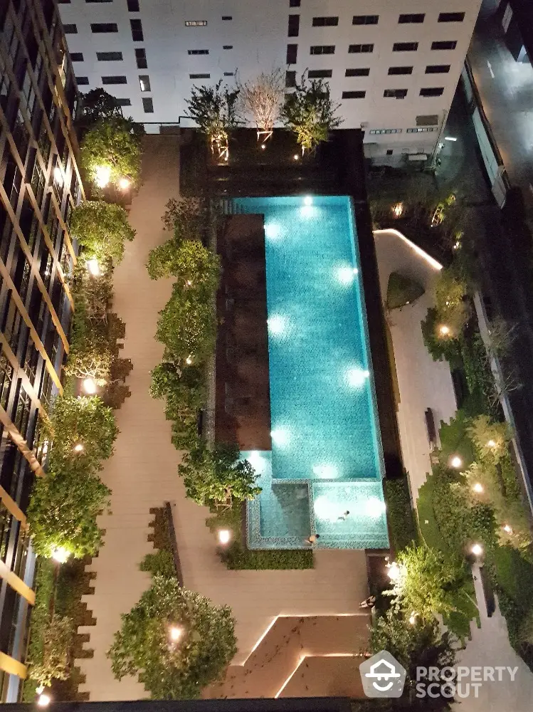 Stunning aerial view of illuminated modern apartment pool area at night with lush greenery.