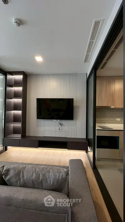 Modern living room with sleek TV setup and view into stylish kitchen