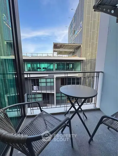Modern balcony with city view, featuring stylish outdoor furniture and glass railings.