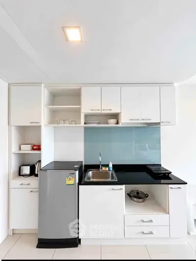 Modern compact kitchen with sleek white cabinets and black countertop, featuring a mini fridge and electric stove.