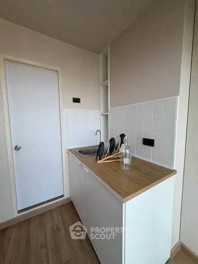 Compact kitchen with sleek white cabinets and wooden countertop, featuring a minimalist design and modern fixtures.