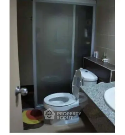 Compact bathroom with modern fixtures and sliding shower door, featuring a granite countertop and colorful rug.