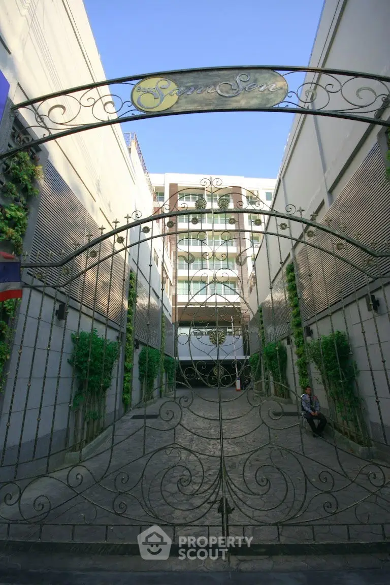 Elegant gated entrance to a modern residential building with lush greenery.