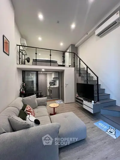 Modern loft-style living room with mezzanine, cozy gray sofa, and sleek kitchen area.