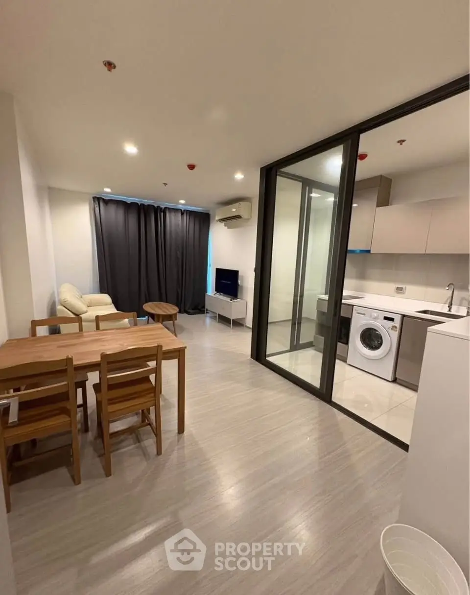 Modern open-plan living room with kitchen and washing machine, featuring sleek furniture and neutral tones.