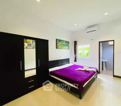 Spacious bedroom with modern decor and ensuite bathroom, featuring a large wardrobe and air conditioning.