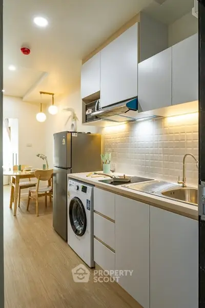 Modern kitchen with sleek cabinetry, washing machine, and dining area in a stylish apartment.