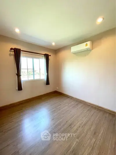 Spacious empty room with wooden flooring and large window, perfect for customization.