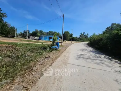 Scenic rural road with lush greenery and a distant blue building under a clear sky.