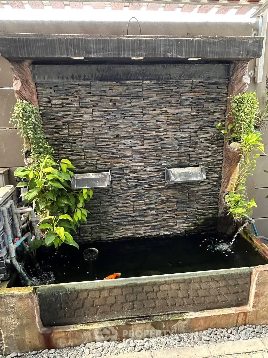 Charming outdoor water feature with stone wall and lush greenery, perfect for enhancing garden aesthetics.