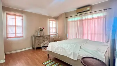 Cozy bedroom with wooden flooring and soft pink curtains, featuring a classic dresser and air conditioning.