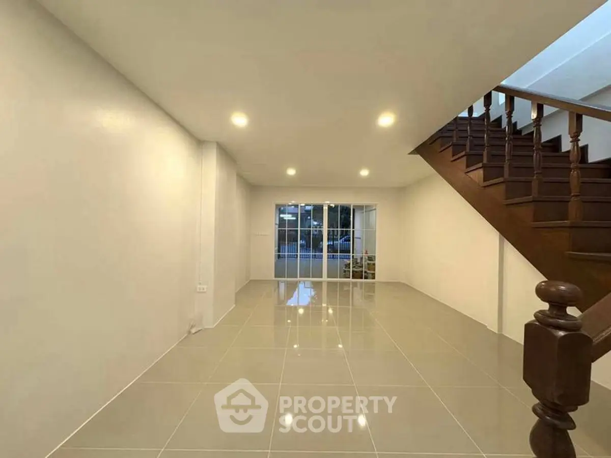 Spacious open-plan living area with glossy tiled floors and elegant wooden staircase.