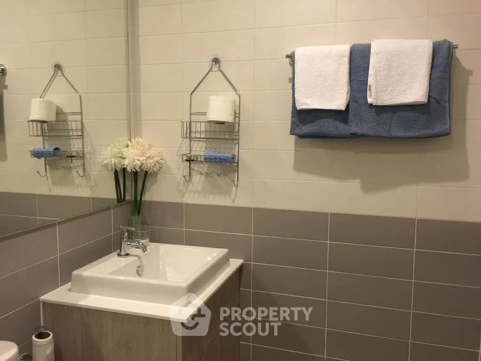 Modern bathroom with elegant sink and towel rack, featuring neutral tiles and decorative flowers.