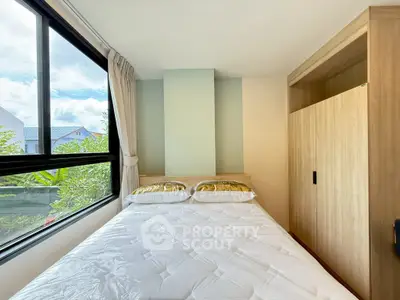 Cozy bedroom with large window and built-in wardrobe, offering a serene view and ample natural light.