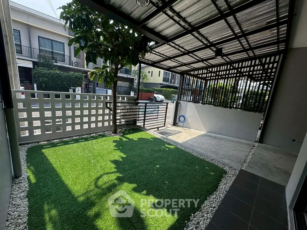 Charming townhouse exterior with covered parking and lush artificial grass area.