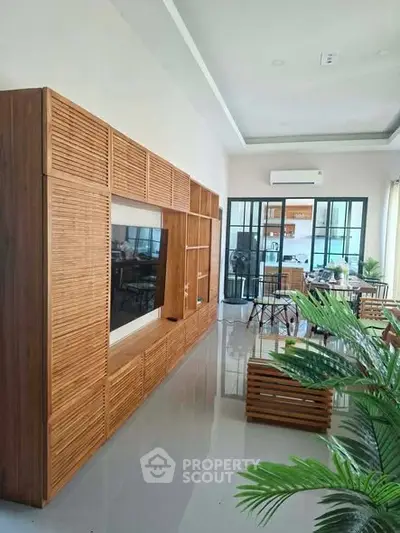 Modern living room with sleek wooden furniture and glass doors leading to a bright dining area.