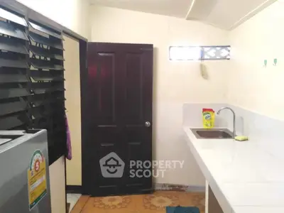 Compact kitchen with white countertop and sink, featuring a fridge and louvered windows.