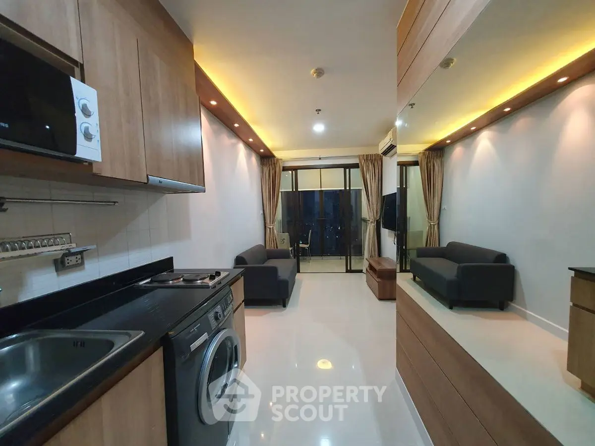 Modern open-layout living room with kitchen, featuring sleek furniture and balcony access.