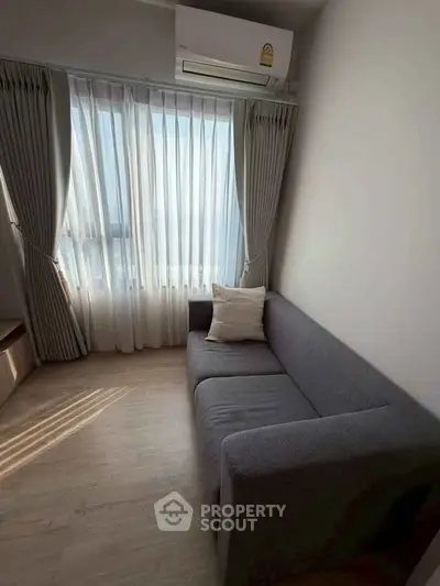 Cozy living room with a modern gray sofa and large window with curtains, perfect for relaxation.