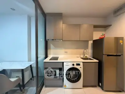 Modern kitchen with washing machine, microwave, and fridge in compact apartment.