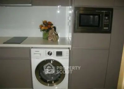 Modern kitchen with built-in appliances including washing machine and microwave, sleek cabinetry, and floral decor.